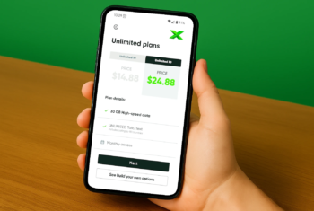 A person holding a smartphone displaying the MobileX Unlimited plans page, showing $14.88 and $24.88 pricing options with plan details, against a green background and wooden desk.