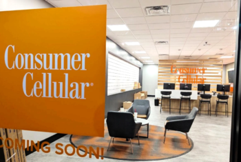 Consumer Cellular retail store interior with orange Consumer Cellular signage, customer seating area, and service counters labeled “Coming Soon.”