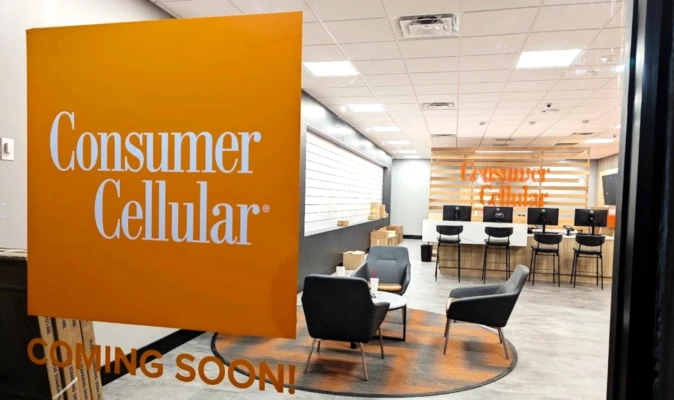 Consumer Cellular retail store interior with orange Consumer Cellular signage, customer seating area, and service counters labeled “Coming Soon.”