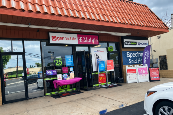 Multi-carrier wireless store displaying Gen Mobile, T-Mobile, Simple Mobile, Ultra Mobile, and Spectrum signage, with phone plan promotions in the windows and outside the entrance.